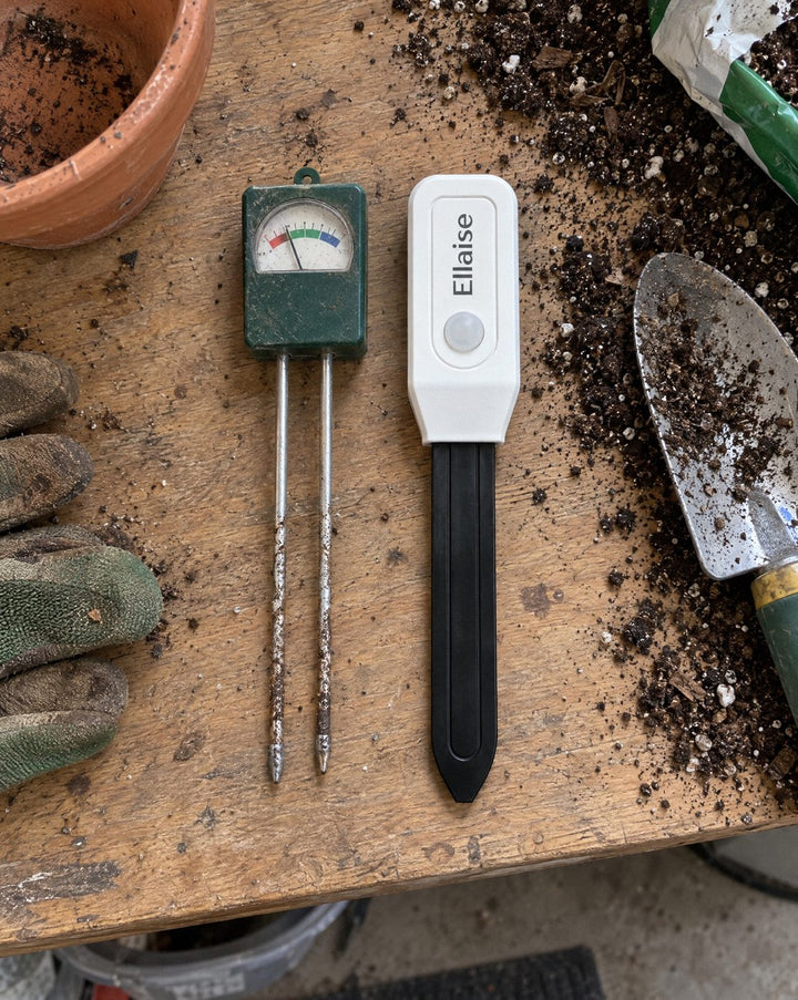 A cheap meter with two metal prongs lying next to Ellaise on a potting bench.