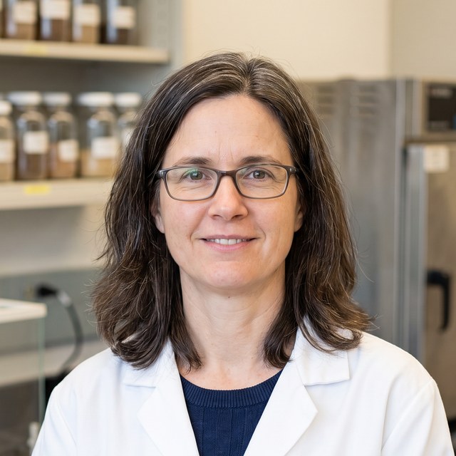 Headshot of Dr. Karen Whitfield. Woman in her 40s in a soil laboratory, lab coat.